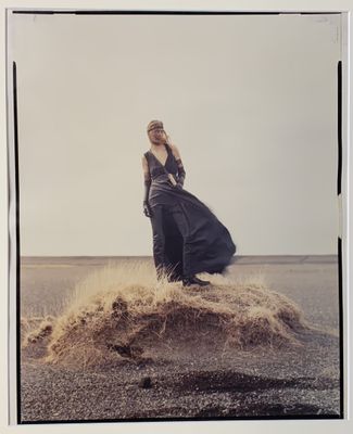 une vieille photo représentant une femme en robe longue, debout au sommet d'un tas de sable