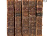 six old books are lined up in a row on a white surface