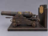 a small wooden cannon on a stand with a book