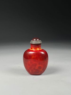 a red vase with a silver lid sitting on a white surface