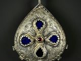 un pendentif en argent richement orné, avec des pierres bleues et rouges sur fond noir