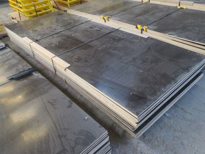 Plusieurs pièces d'acier sont empilées sur des palettes dans un entrepôt