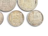 six silver coins of different shapes and sizes on a white surface