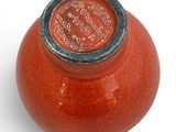 a red vase with a black lid sitting on a white surface