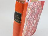 un livre rouge orné d'une étiquette noire, posé sur une surface blanche
