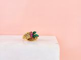 un gros plan d'une bague en or sertie de pierres vertes et roses