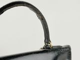 the handle of a black purse with a gold clasp on it