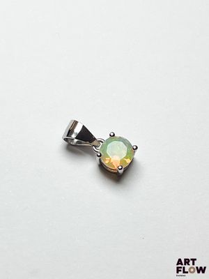 une image représentant un pendentif en cristal vert et jaune posé sur une surface blanche