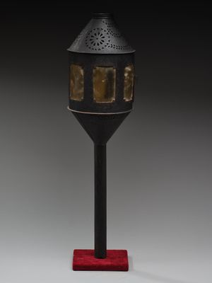 une lampe noire et dorée avec un pied rouge posée sur une surface blanche