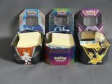 Trois boîtes de cartes Pokémon sont alignées sur une table