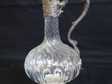un pichet ancien en verre plaqué argent, posé sur un socle, sur fond noir