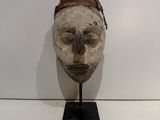 a wooden mask on a black stand on a white wall