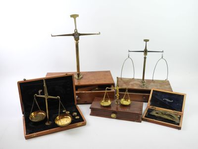 three brass scales and a wooden box on a white surface