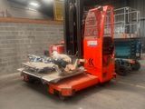 a red forklift in a warehouse with a blue truck in the background