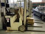 un chariot élévateur dans un entrepôt, avec une voiture en arrière-plan