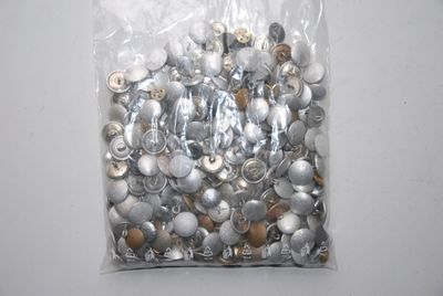 un sachet de boutons argentés et dorés posé sur une table blanche