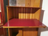 a wooden desk with a red top in the corner of a room