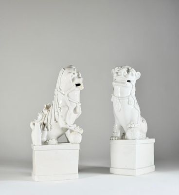 une paire de statues de lions blanches sur des socles, sur fond gris