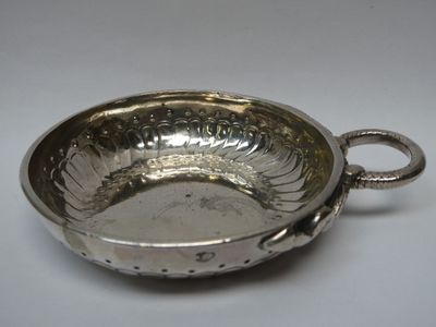une assiette en argent antique avec une poignée sur une surface blanche