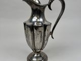 an antique silver plated pitcher on a stand on a white background