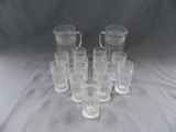 six pichets en verre transparent et un pichet posé sur une nappe blanche