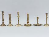 six brass candlesticks are lined up on a white surface