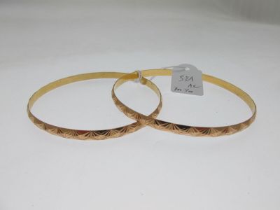 two gold bracelets with engraved designs on them sitting on a white surface
