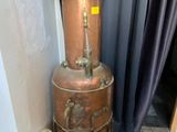a tall copper pot sitting next to a fan