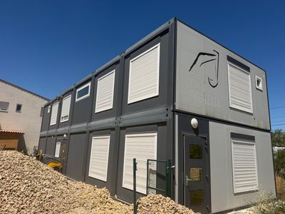 une maison-conteneur posée sur un tas de pierres devant un immeuble