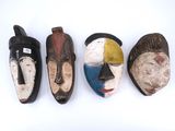 four wooden masks are lined up on a white surface