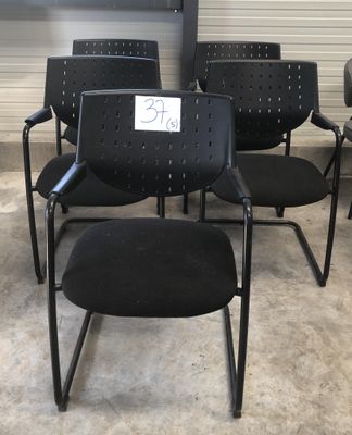 Plusieurs chaises noires sont alignées en rangée, avec une pancarte fixée sur le dossier.