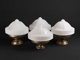 trois lampes en verre blanc avec des pieds dorés sur fond noir