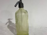 a green glass bottle with a black handle on a white surface