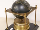 a black and gold globe on a stand with a painting in the background
