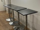 trois tables noires avec des pieds chromés dans une pièce