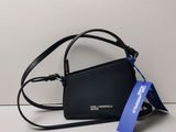 un sac à main noir orné d'une étiquette bleue, posé contre un mur blanc
