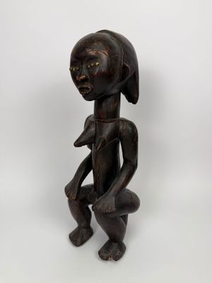 une statue en bois représentant une femme, la main posée sur la poitrine