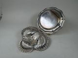 two silver dishes on a white table with a clock in the background