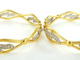 deux boucles d'oreilles pendantes en or et diamants blancs posées sur un fond blanc