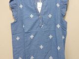 a blue top with white embroidery on it hanging on a hanger