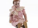 an old doll sitting on the ground wearing a pink dress and brown shoes