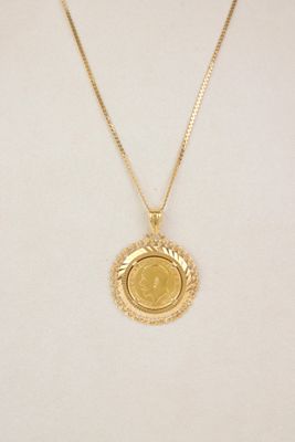a gold necklace with a coin on a mannequin neck
