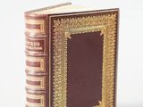 an old book with gold trim and a brown cover sitting on a white surface