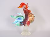 une figurine en verre représentant un coq, posée sur un socle transparent