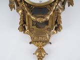 a gold clock hanging on the wall with a white background