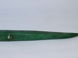une vieille pipe verte avec un manche en bois, posée sur une surface blanche
