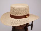 chapeau de paille beige orné d'un ruban en cuir marron, posé sur un support en bois