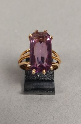 une image représentant une bague ornée d'une pierre violette posée sur un socle noir
