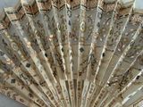 a white fan with gold designs on it sitting on a table