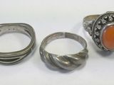 three silver rings and a ring with an orange stone